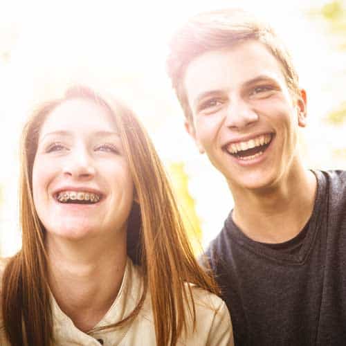 A teenage girl and boy smiling brightly in sunlight.