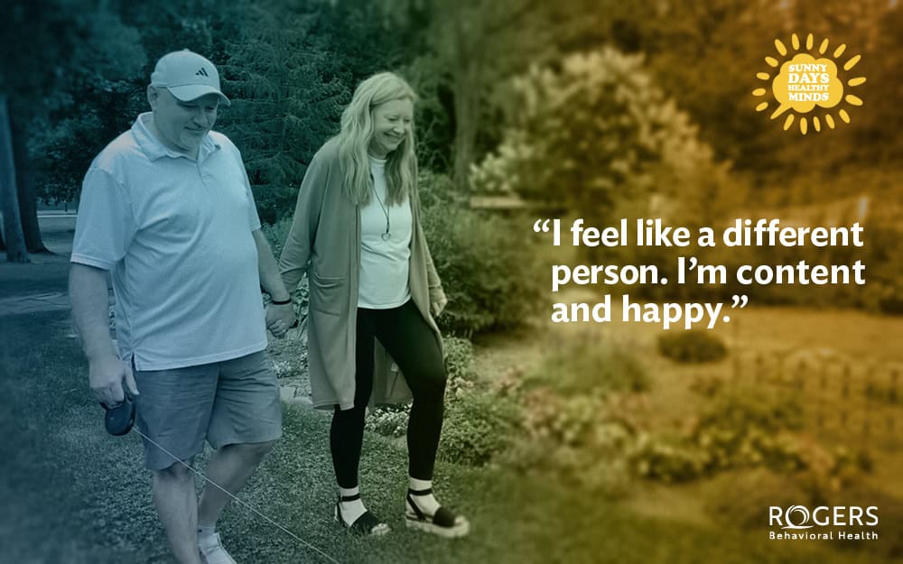 The image shows a man and a woman walking hand-in-hand along a path in a garden setting. The man on the left is wearing a light polo shirt, shorts, and a cap, and he is holding a retractable dog leash. The woman on the right is wearing a long cardigan, a white top, and black pants. She appears to be smiling. The background features lush greenery, with tall trees and various plants. In the upper right corner, there is a graphic of a sun with the words "Sunny Days Healthy Minds" written inside. A quote overlays the image on the right: “I feel like a different person. I’m content and happy.”