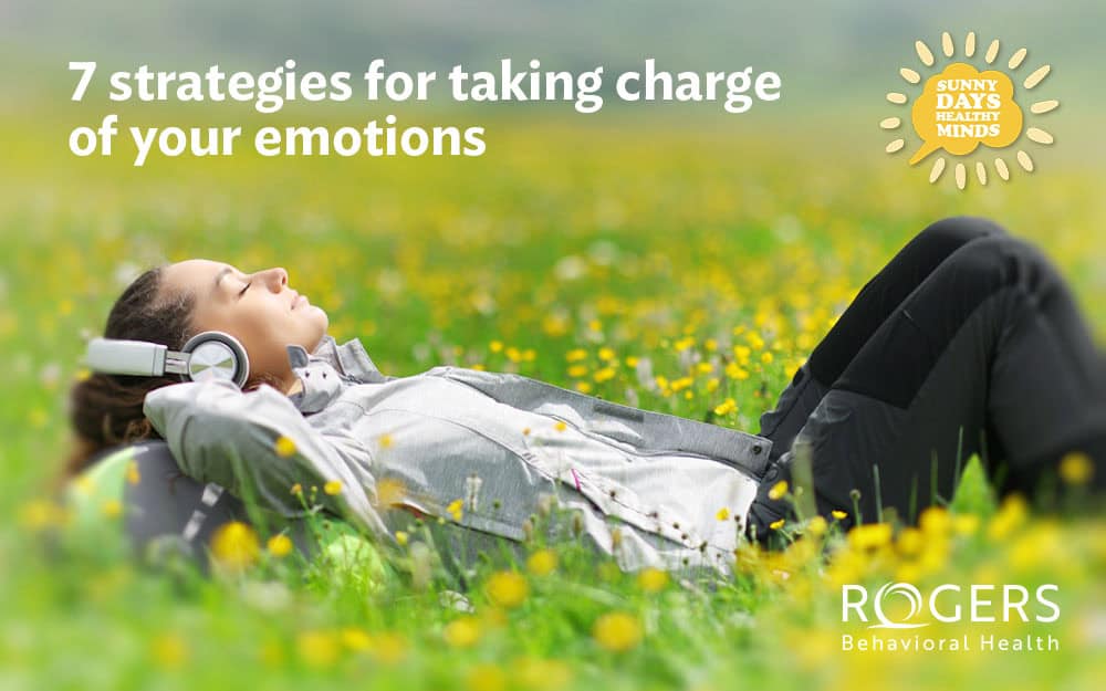 dotted with yellow and white flowers. They are wearing a light gray top and dark pants, with headphones resting on their ears. The person appears relaxed, with their eyes closed and arms behind their head. In the top-left corner, white text reads, "7 strategies for taking charge of your emotions." In the top-right corner, a yellow sun icon contains the words "Sunny Days Healthy Minds" in a circular pattern.