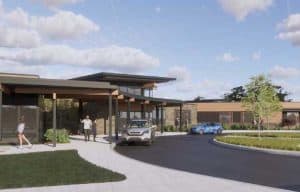 A modern building with a glass and wood facade, a circular driveway with parked cars, and scattered clouds in the sky.