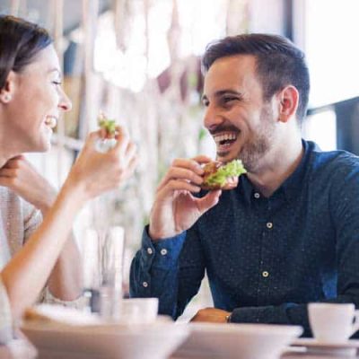 Two people joyfully eating together at a table indoors.